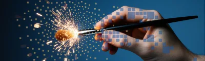 A hand holding a paintbrush against a blue background, with sparks bursting from the brush tip and translucent pixel squares dissolving across the hand.